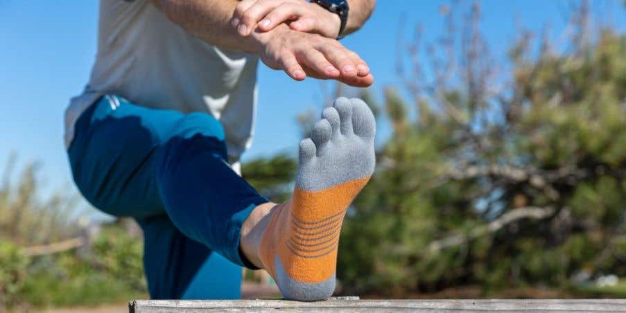 A person using a wooden bench to stretch his fingers to his toes, wearing Injinji Run Lightweight No-Show toesocks.