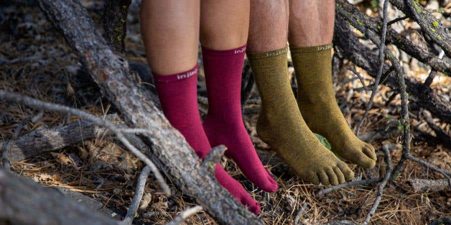 Two people sitting on a downed tree wearing Injinji Liner Crew performance toesocks.
