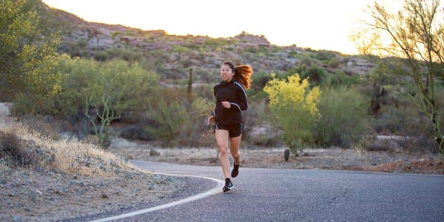 Woman running down a paved path surrounded by plants and bushes. 