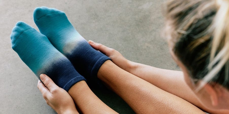 A person sitting on their floor leaning over their legs and stretching their hands to their toes while wearing Injinji x Pointe Studio Grip Full Foot No-Show socks.