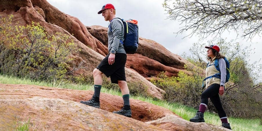 Two hikers carrying backpacks and walking up a hill on a trail.