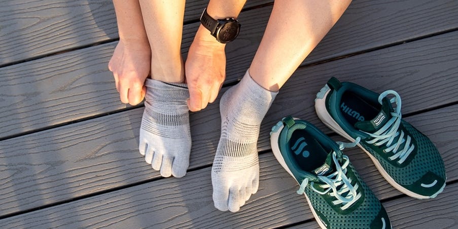 A person sitting down their feet adjusting their Injinji Run Lightweight Mini-Crew toesocks with their running shoes resting next to them.