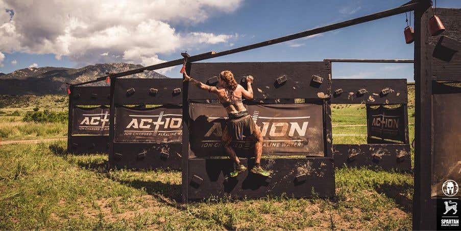 A female athlete climbing up a wooden barricade.
