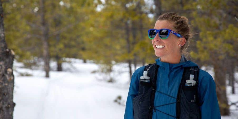 Courtney Dauwalter standing in a snowy forest wearing Injinji x Knockaround sunglasses.