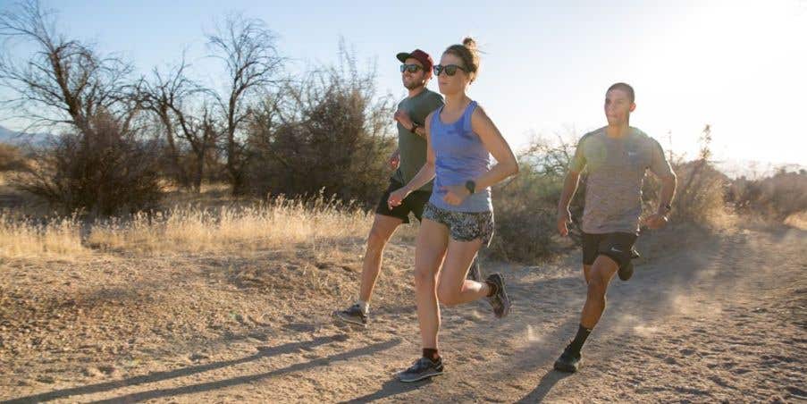 Three people running on a wide sandy trail.