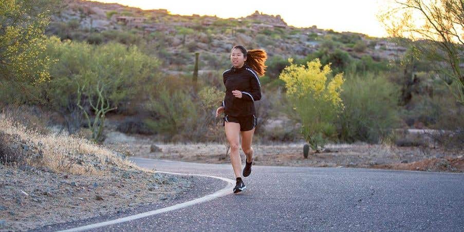 An young woman running on a curved desert road in the late afternoon. 