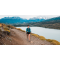 Team Injinji athlete Skye Stoury walking on a trail situated on the edge of a wide river with mountains in the background.