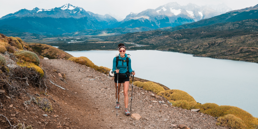 Team Injinji athlete Skye Stoury walking on a trail situated on the edge of a wide river with mountains in the background.