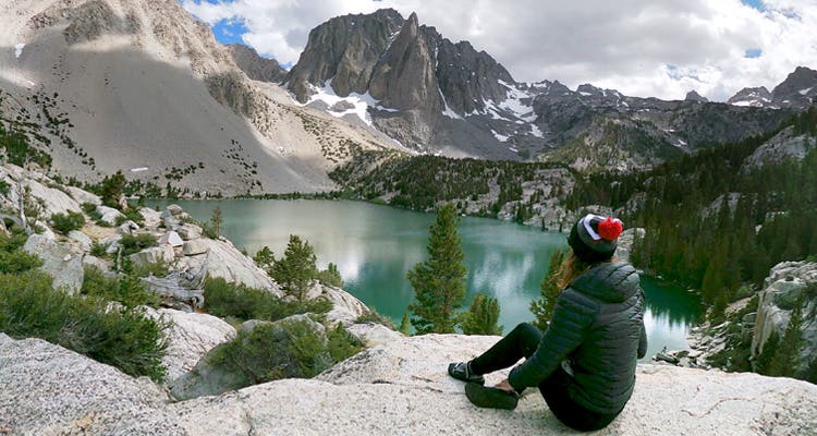 A women sitting on a rock looking at a mountain view wearing an Injinji Beanie in gray, red, black and white