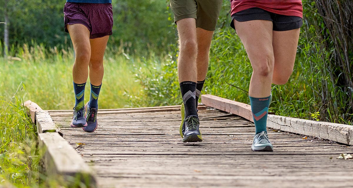 Runners crossing a trail bridge wearing Injinji Run Lightweight Crew Socks in Glow, Black and Lagoon.