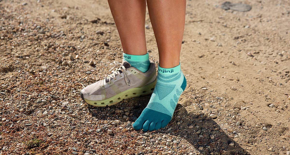 A woman standing on a rail with one running sneaker on and one off, wearing Injinji Women's Ultra Run Mini-Crew toesocks in Glacier