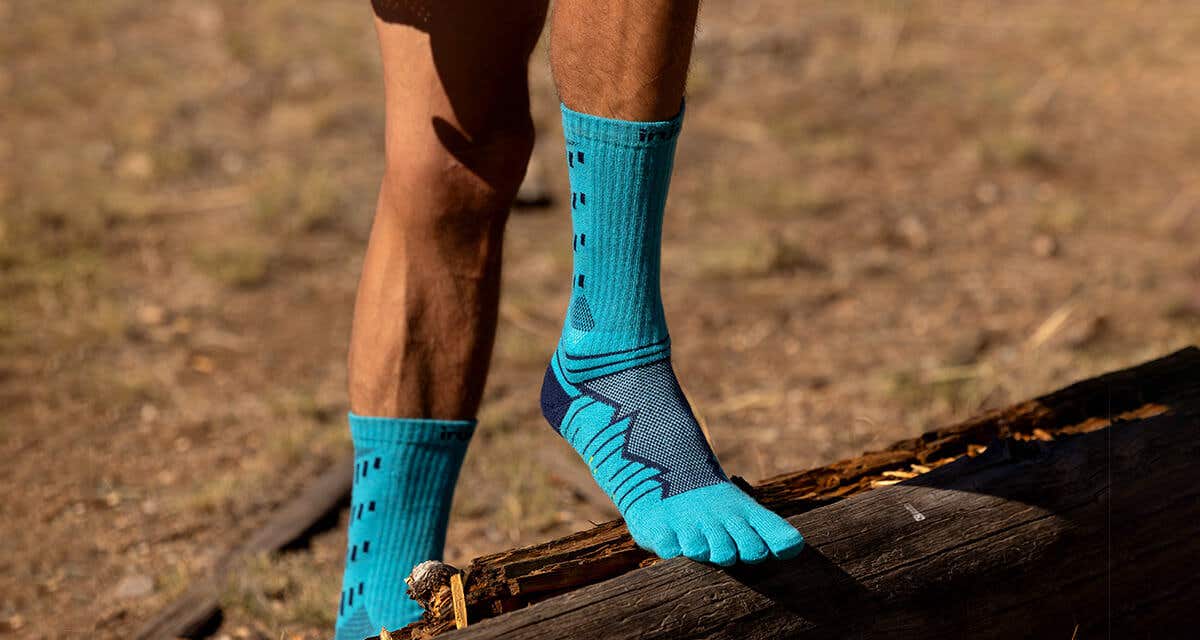 A man with one foot up on a downed log wearing Injinji Ultra Run Crew toesocks in Pacific Blue