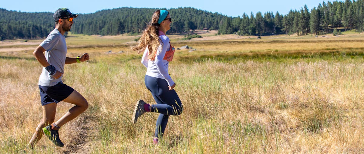 A man and woman in running apparel running on a trail in an open meadow wearing Injinji Trail Midweight Mini-Crew running toesocks.