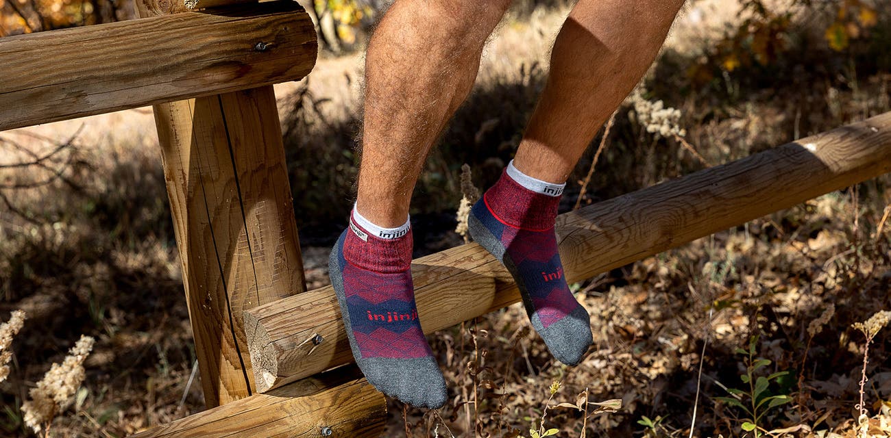 Man sitting on a fence wearing the new bugundy colored Injinji Liner + Runner dual sock system. 