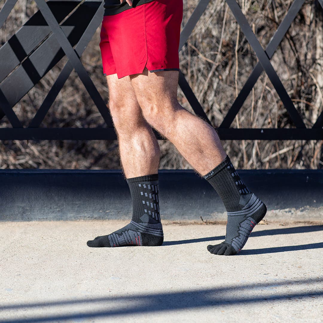 A man in gym apparel standing outdoors wearing the Injinji Ultra Run Crew sock in Obsidian.