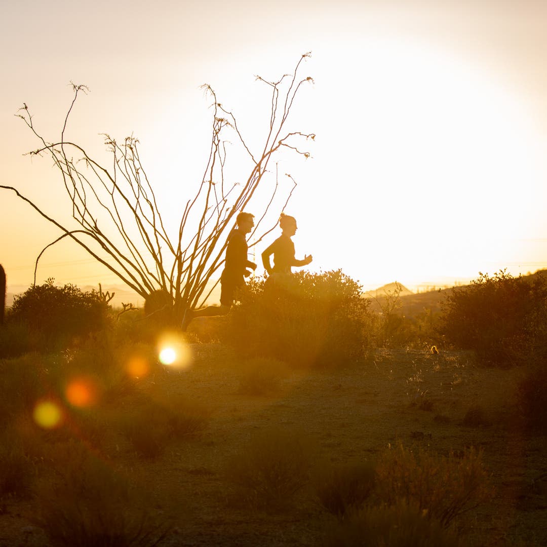 Two people running on a trail in the desert at dusk. 