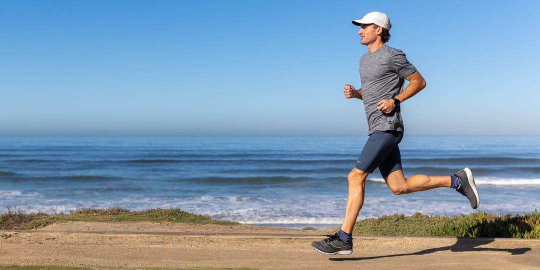 A man running along a flat dirt trail in front of the ocean.