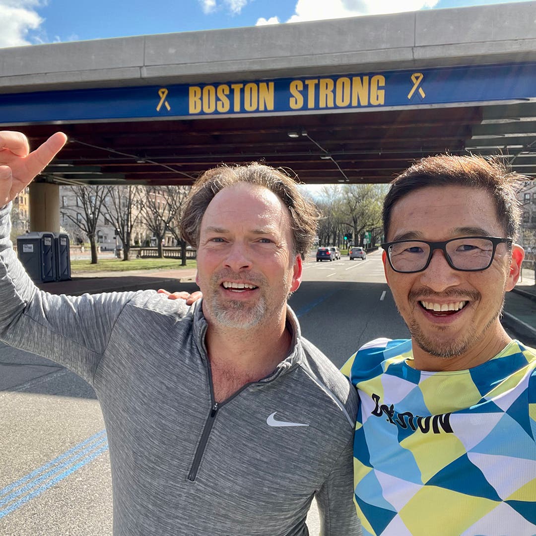 Team Injinji athlete Phil Shin with his good friend Murph standing and pointing at the blue Boston Strong sign at the Boston Marathon.