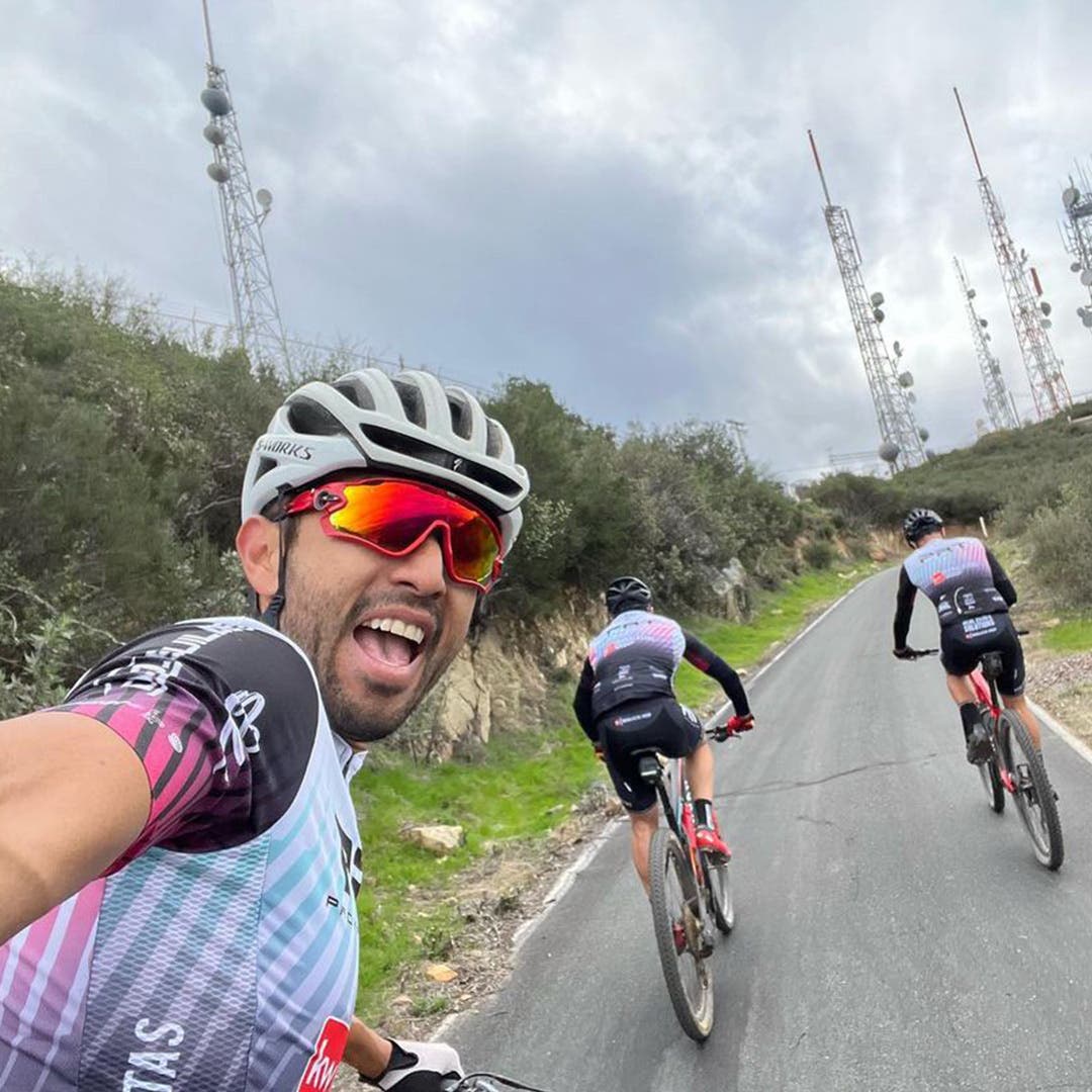Team Injinji Athlete Jesus Topete Jr. taking a selfie while riding his bike with fellow cyclists down a long paved path.