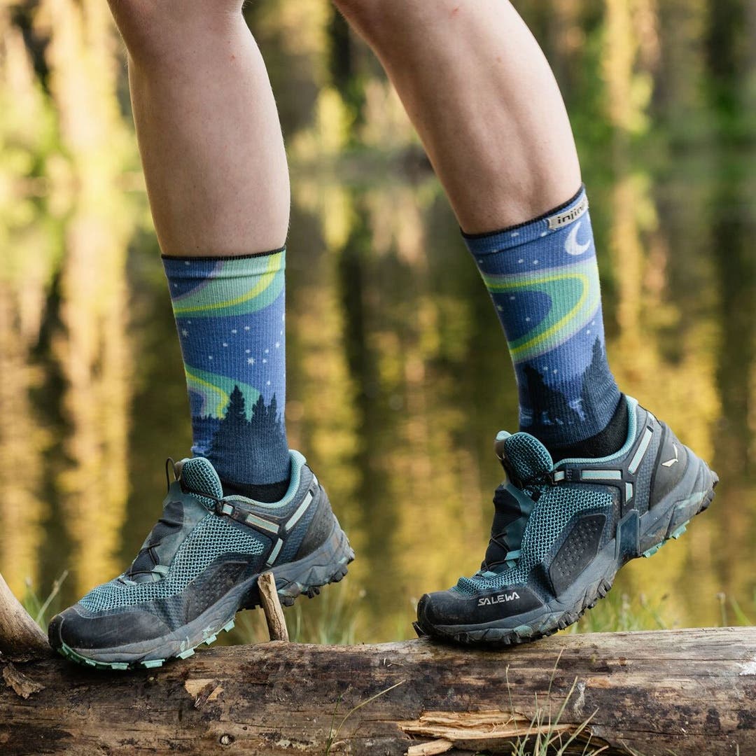 A person balancing on a log in front of a lake wearing Injinji Artist Designed Women's Crew toesocks in Howl.