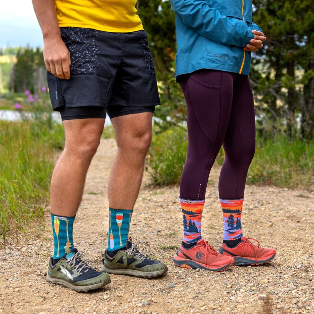 Two people standing on a Trail in front of a lake wearing Injinji Artist Designed toesocks in Oars and Dusk.
