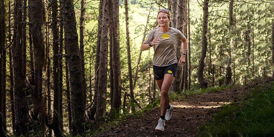 Team Injinji Athlete Alyssa Clark running on a trail through a dense forest.