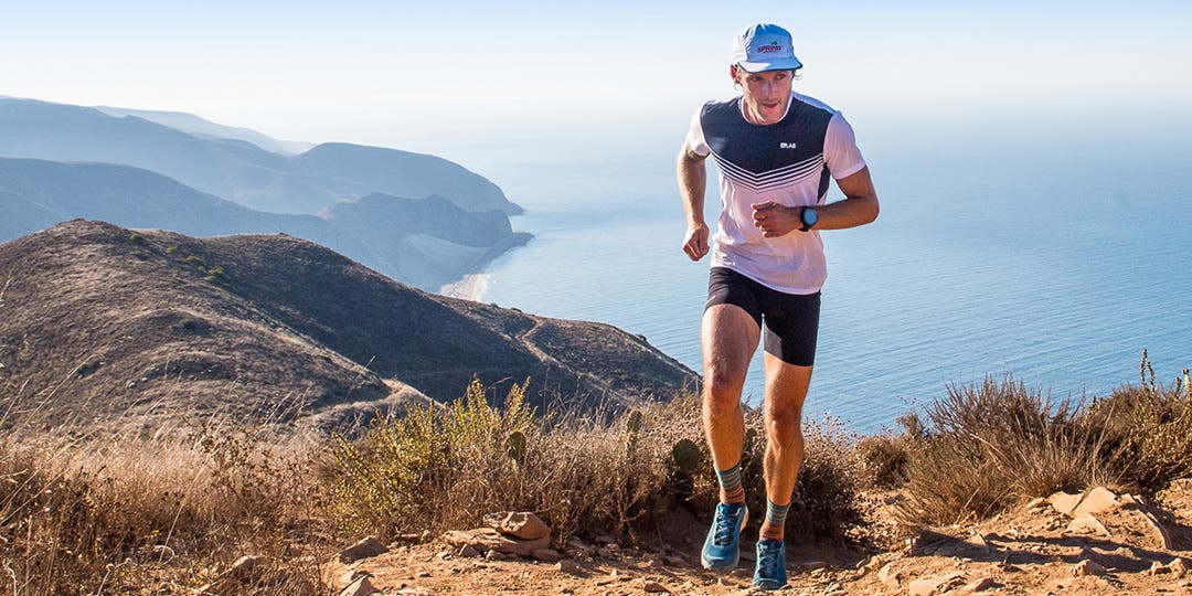 Male trail runner sitting on a wooden bench putting on his running shoes wearing crew length ultra-run toesocks. 