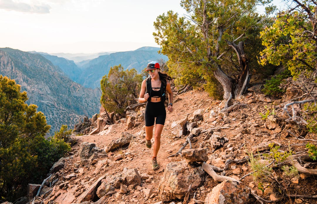 Trailer Runner running along a desert cliff trail wearing the Injinji Trail Cap.