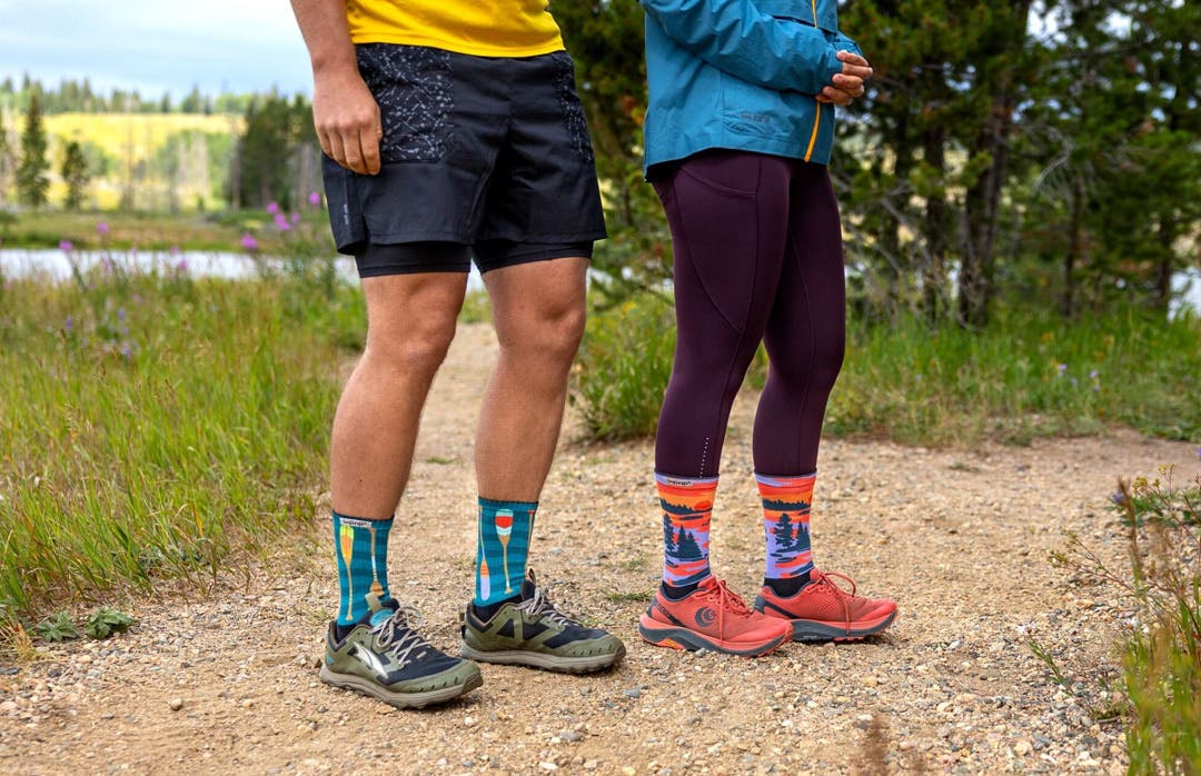 Two people standing on a Trail in front of a lake wearing Injinji Artist Designed toesocks in Oars and Dusk.