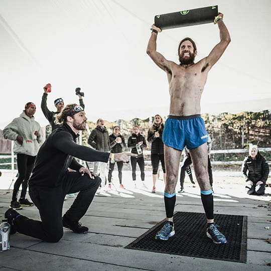 Ultra runner Mike Wardian surrounded by a crowd holds a heavy block above his head