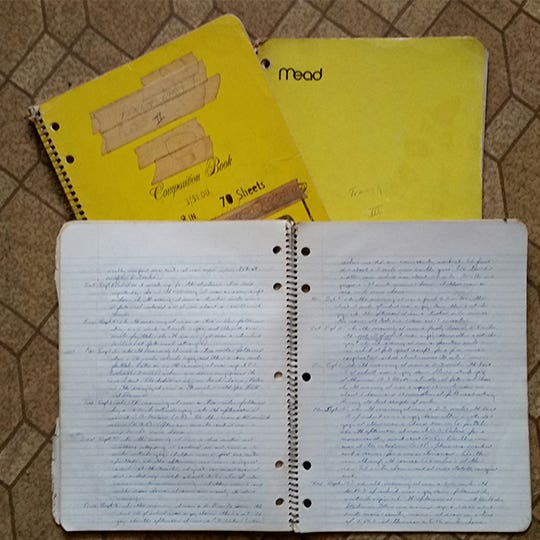 Open notebook full of writings laying on two other yellow notebooks