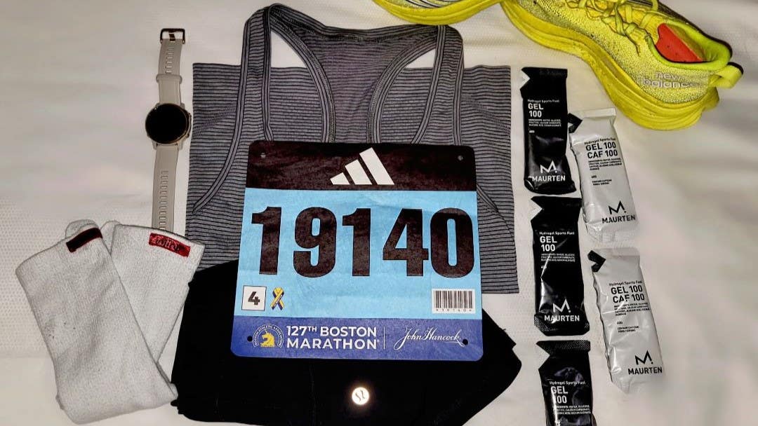 A race bib, Injinji Sport socks, running energy gels, neon running shoes, and a fitness watch laying flat on a bed.
