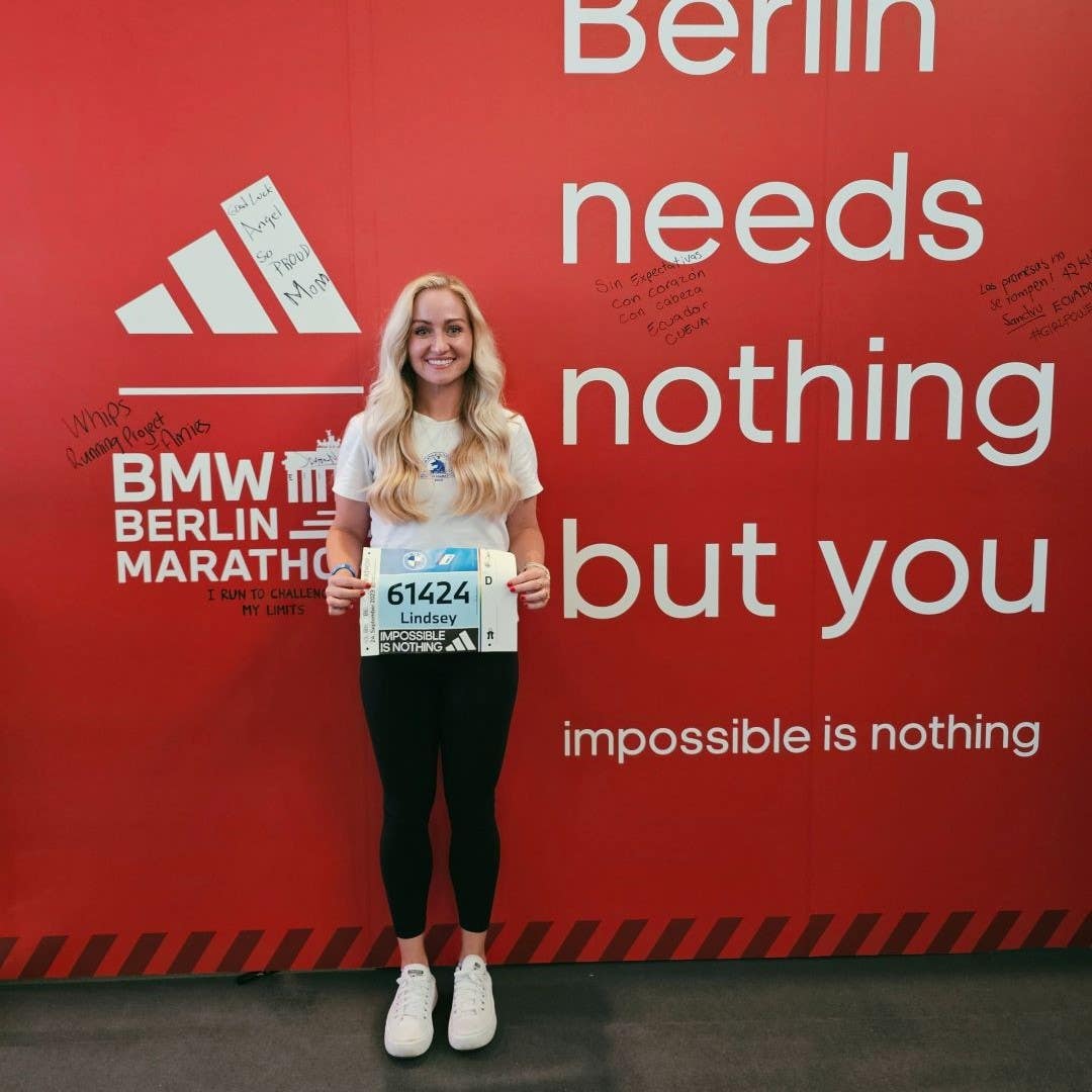 Lindsey LaVeck standing in front of a large red Berlin Marathon advertisement holding her race bib.