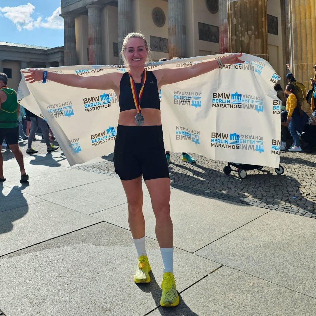 Lindsey LaVeck looking happy and smiling while wearing a Berlin Marathon flag around her body post race.