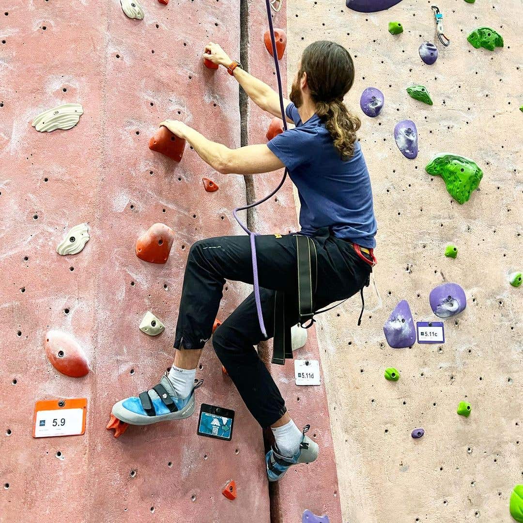 Mike Wardian wearing a climbing harness pulling himself up by rock holds in a climbing gym.