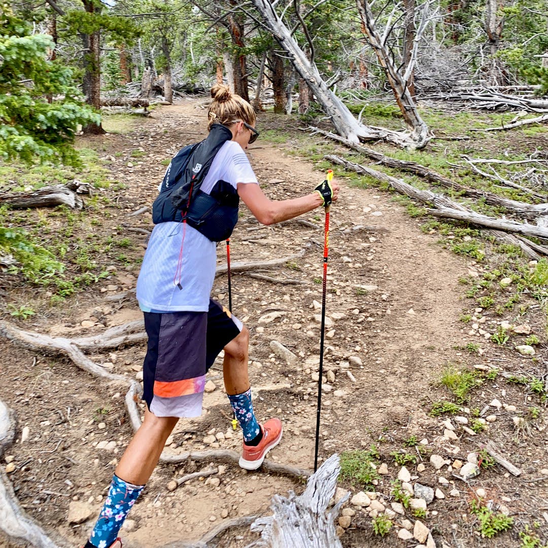 Courtney Dauwalter walking on a trail in the mountains with hiking poles