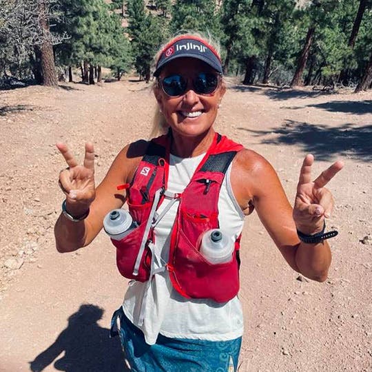 Amy Costa smiling on the trail wearing her hydration vest and Injinji visor. 