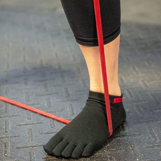 A foot in black Injinji toe socks with an elastic ribbon being stretched around it