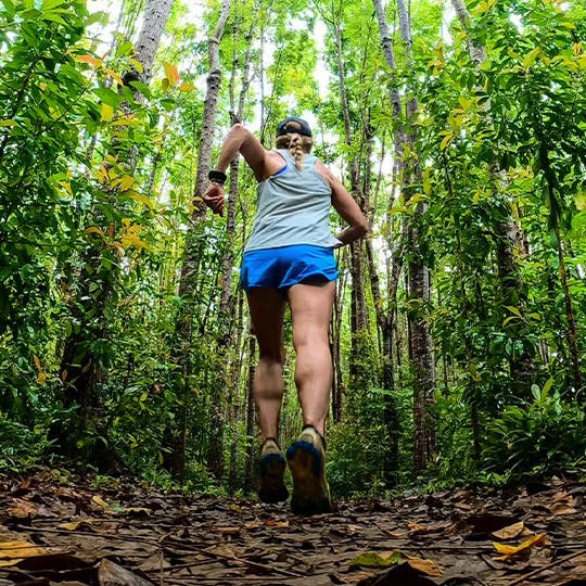 Tara Warren running in the green forest seen from the back