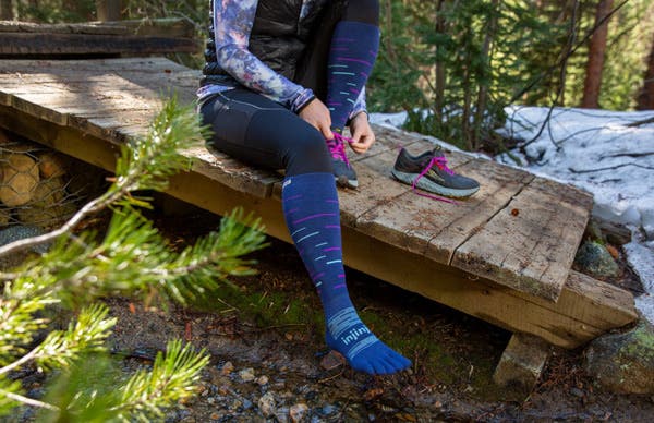Trail Runner finishing putting on the new Injinji Snow Over the Calf toesocks in twilight.