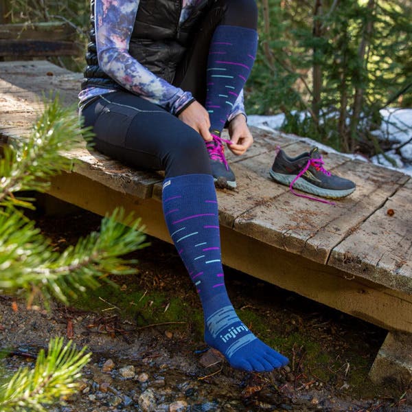 Trail Runner finishing putting on the new Injinji Snow Over the Calf toesocks in twilight.