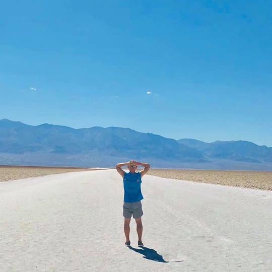 A man standing on the asphalted desertous road and looking at the distant mountain