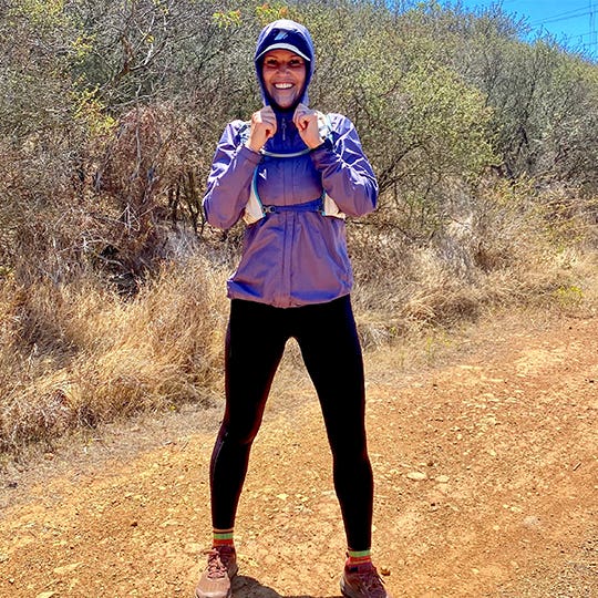 Woman in violet sports jacket and black leggings standing on the sandy road near the bushes