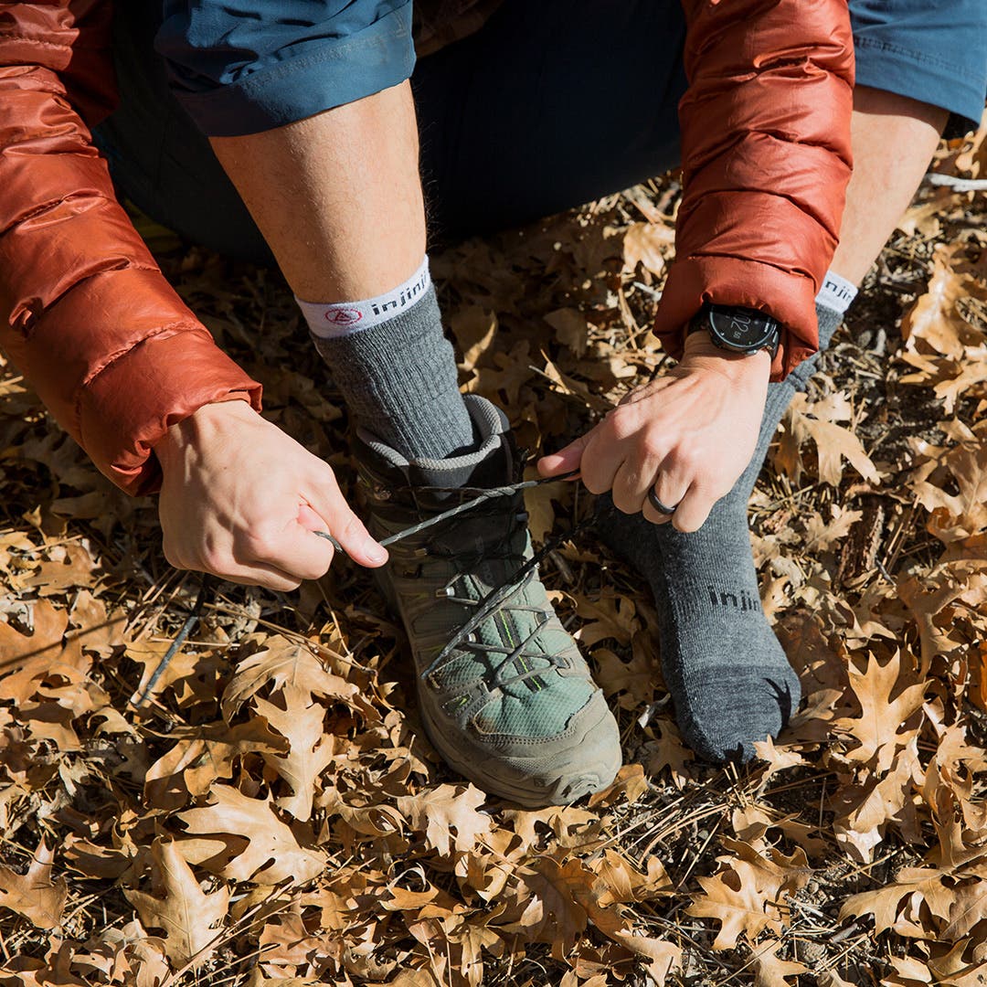 A hiker sitting on the ground among dead leaves putting on their hiking boots.  