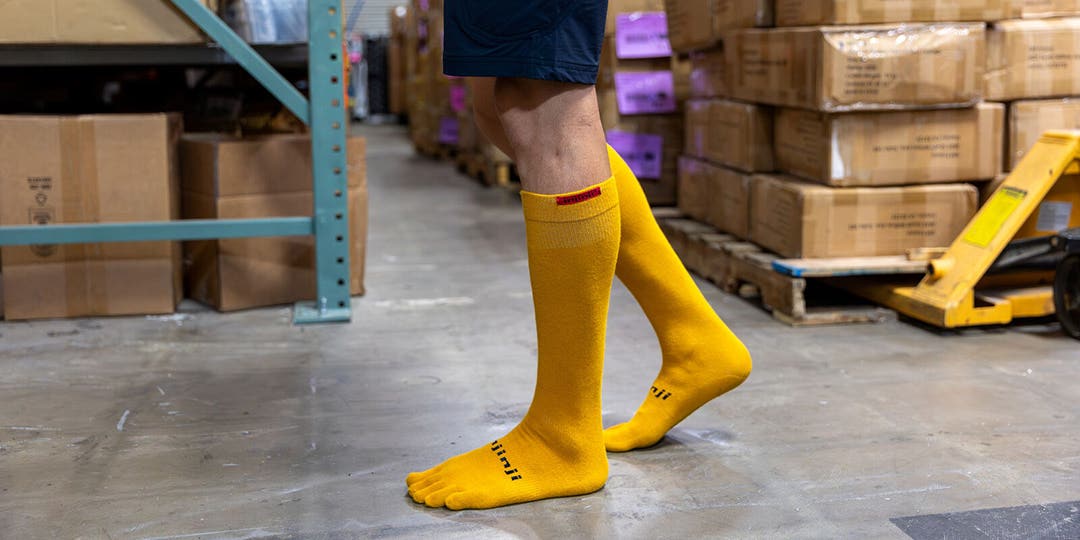 A person among piles of cardboard boxes in a warehouse wearing Injinji Boot Original Weight OTC socks.