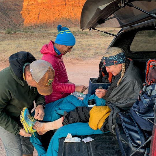 A man is taking the sneaker off Denise Bourassa's foot while she is sitting in the car