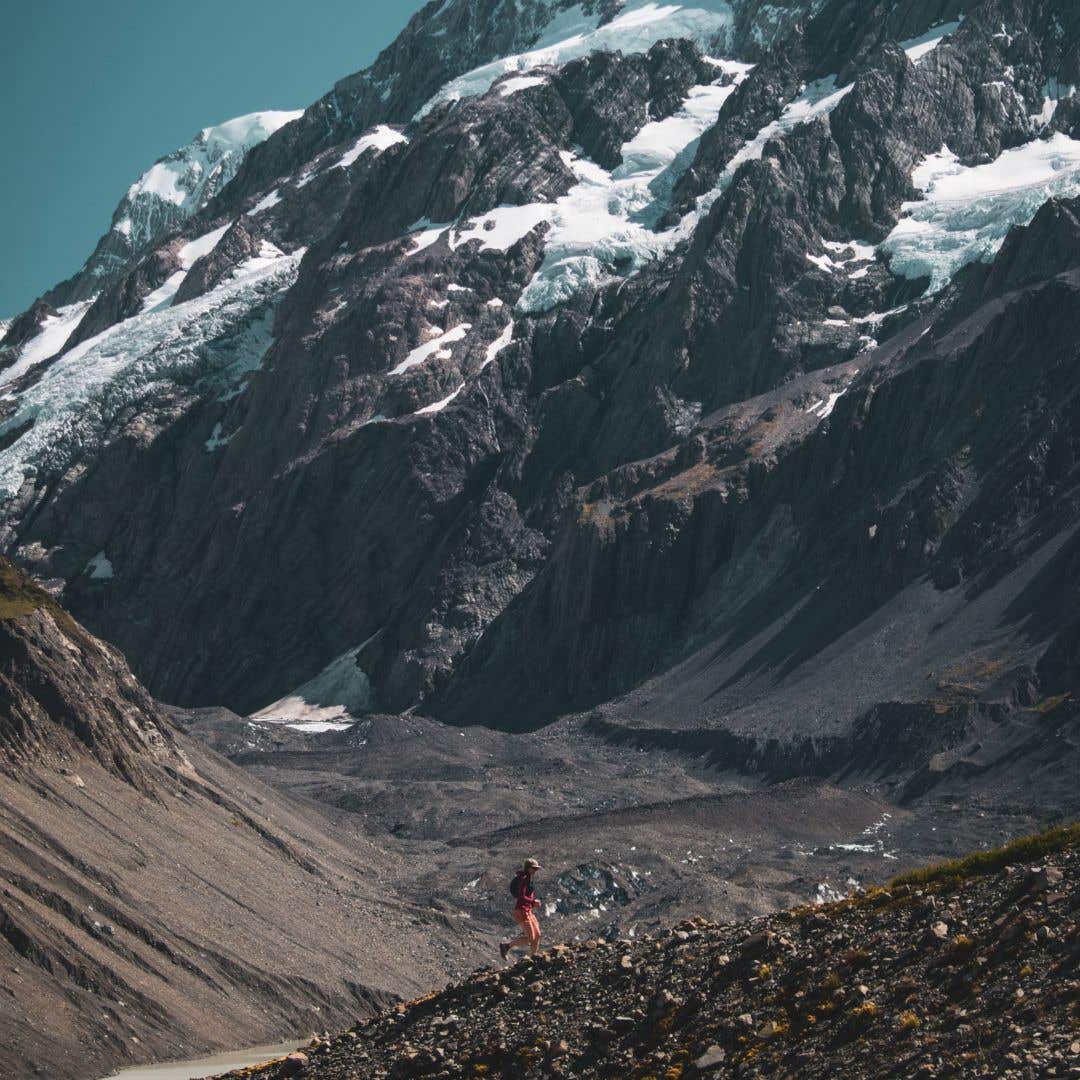 Team Injinji Athlete Caroline Himbert up a rocky incline on a mountain with epic views of mountain peaks behind her.