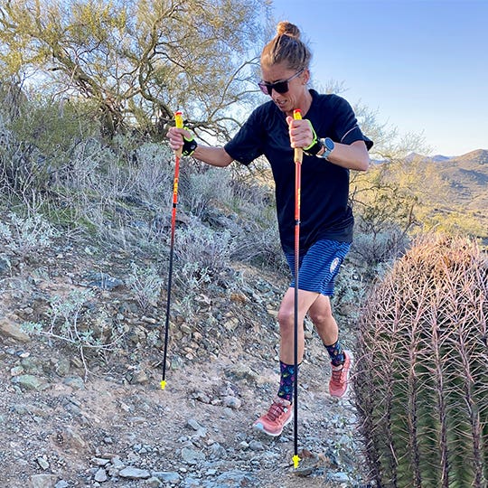 Courtney Dauwalter using poles to hike up a rocky desert trail. 