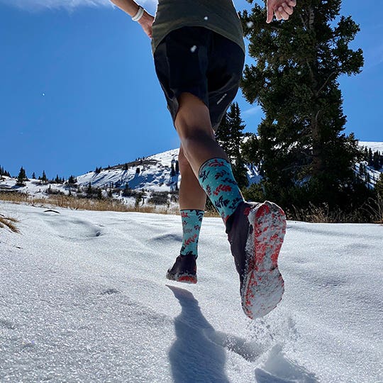 Courtney Dauwalter running in the snow wearing the Spectrum Women's Trail Midweight Crew.