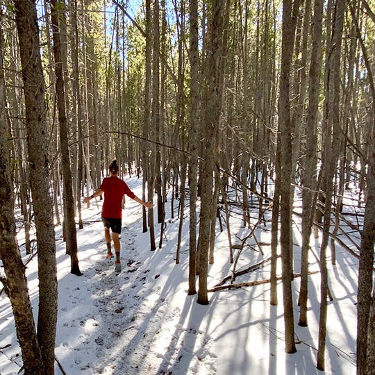 Courtney Dauwalter weaving through trees wearing her Spectrum Women's Trail Midweight Crew.